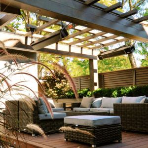 City garden between laneway garage and house has lounge furniture arranged on a ground level deck set beneath a dramatic pergola that spans width of the yard.